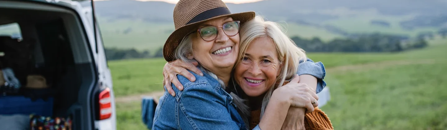 Two older women outside hugging and smiling.