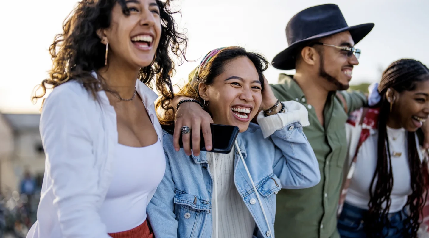 A group of friends with their arms around each other outside laughing together.